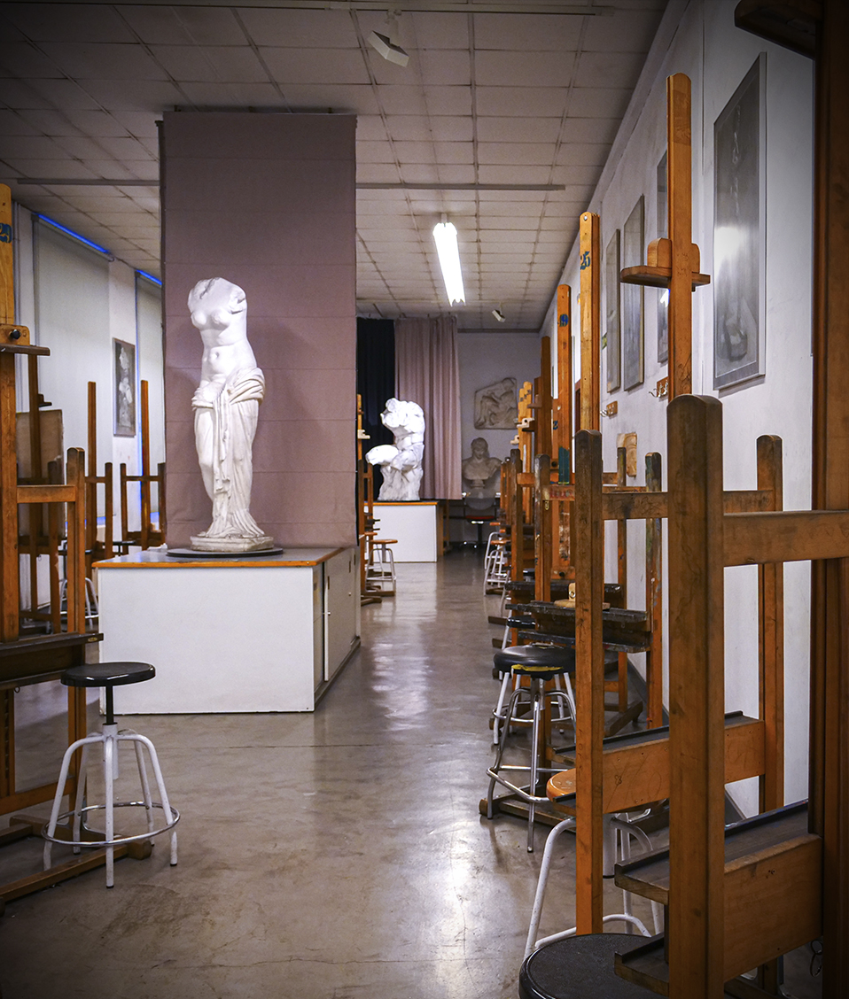 Aula vacía de la Facultad de Bellas Artes con taburetes, caballetes y dos esculturas en el centro