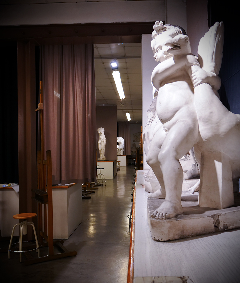 Escultura de un niño con un ganso y al fondo un aula vacía de la Facultad de Bellas Artes